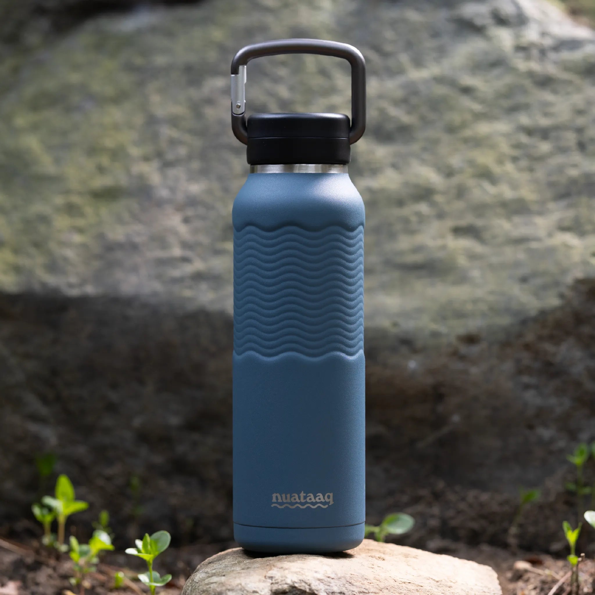 Blue water bottle with a carabiner on a rock against a natural background