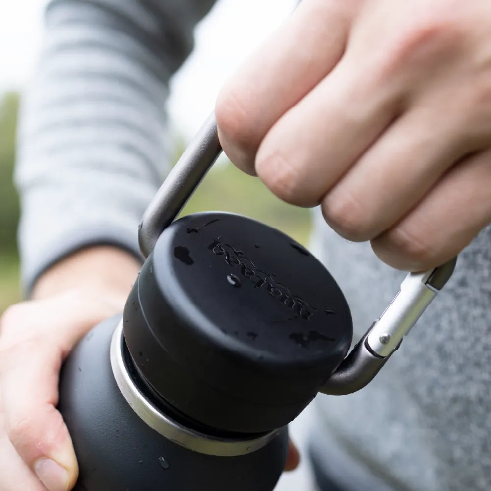 Person holding a black insulated bottle with a carabiner lid outdoors