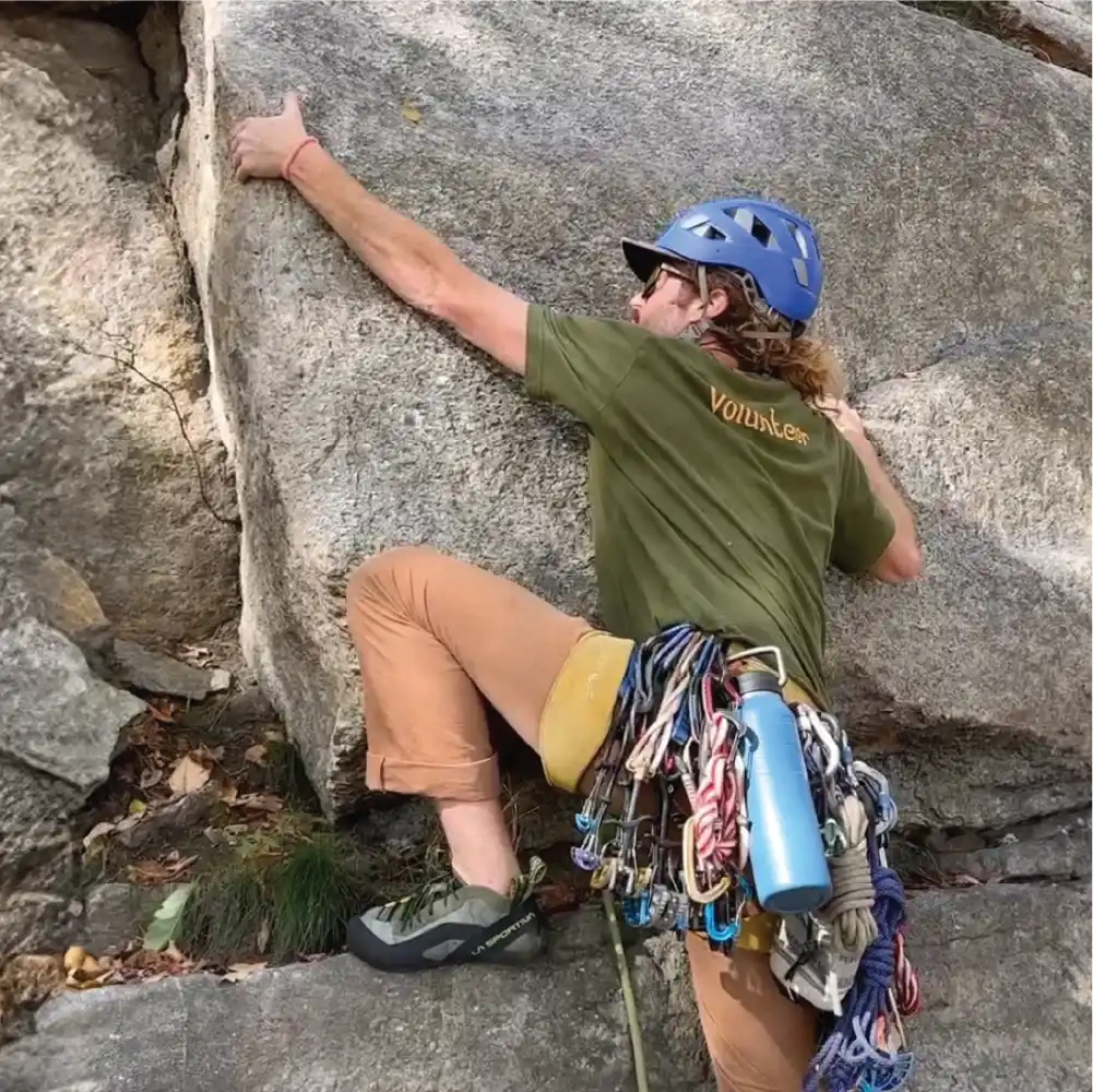 Close up of rock climber with lake blue Nuataaq Carabiner Bottle attached to climbing harness in mountain landscape 