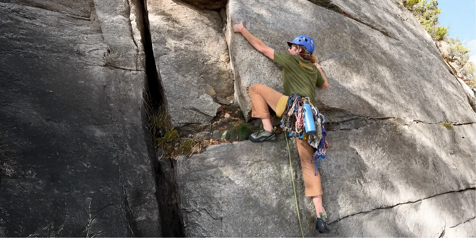 Rock climber with lake blue Nuataaq Carabiner Bottle attached to climbing harness in mountain landscape