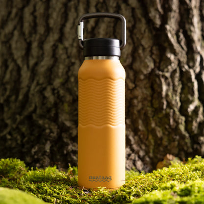 Orange water bottle with black cap on a mossy surface against a tree trunk