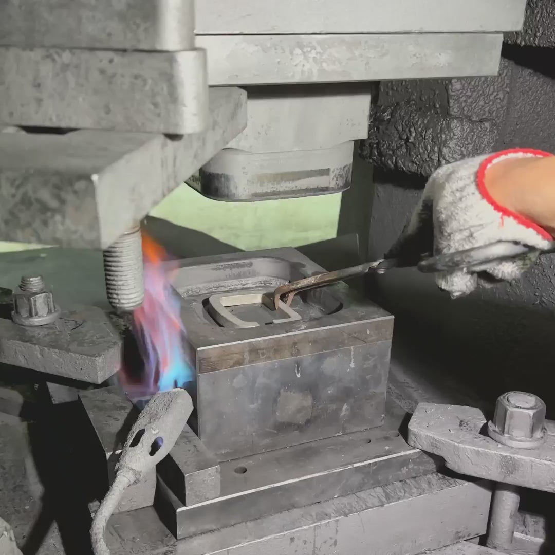 Load video: Video of a nuataaq carabiner being forged, fire is shooting onto the carabiner as a hydraulic press forges the carabiner